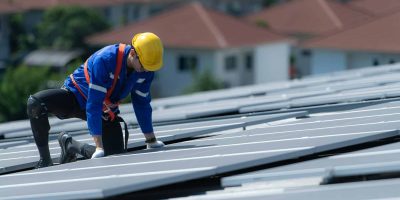 A technician is installing solar panels on the roof of the warehouse